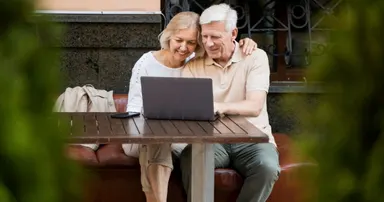 Elderly couple at a bench outside their los altos home while the husband is checking his laptop and conversing with his wife