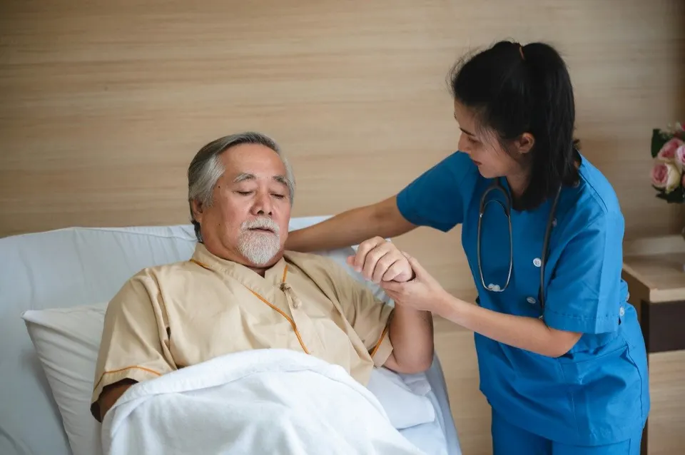 Nurse caring for an elderly man in a hospital bed.